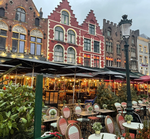 Au&szlig;engastronomie auf einem Platz vor historischen Giebelh&auml;usern in Br&uuml;gge, Belgien, mit gedeckten Tischen und Pflanzen.