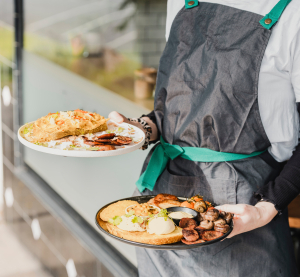 Kellnerin tr&auml;gt zwei Teller mit modernen Gerichten in einem Caf&eacute;, typisch f&uuml;r Melbournes vielf&auml;ltige Food-Szene.