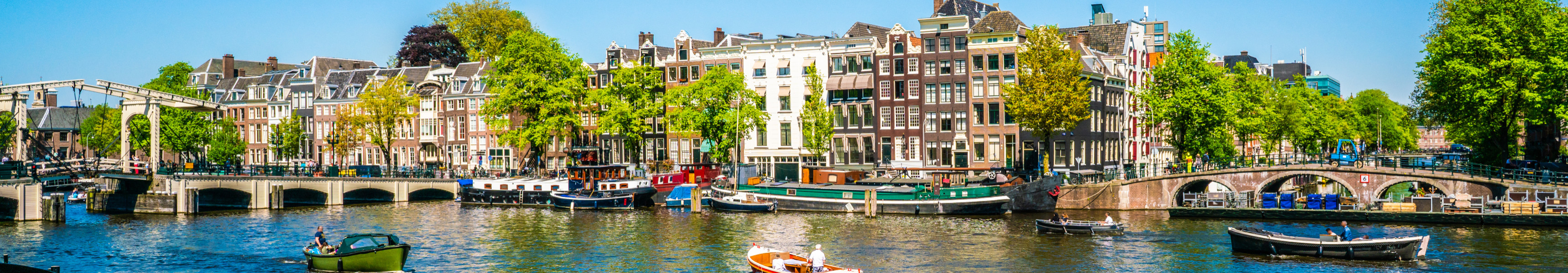 Grachte in Amsterdam mit historischen H&auml;usern, Booten und Br&uuml;cken bei Sonnenschein