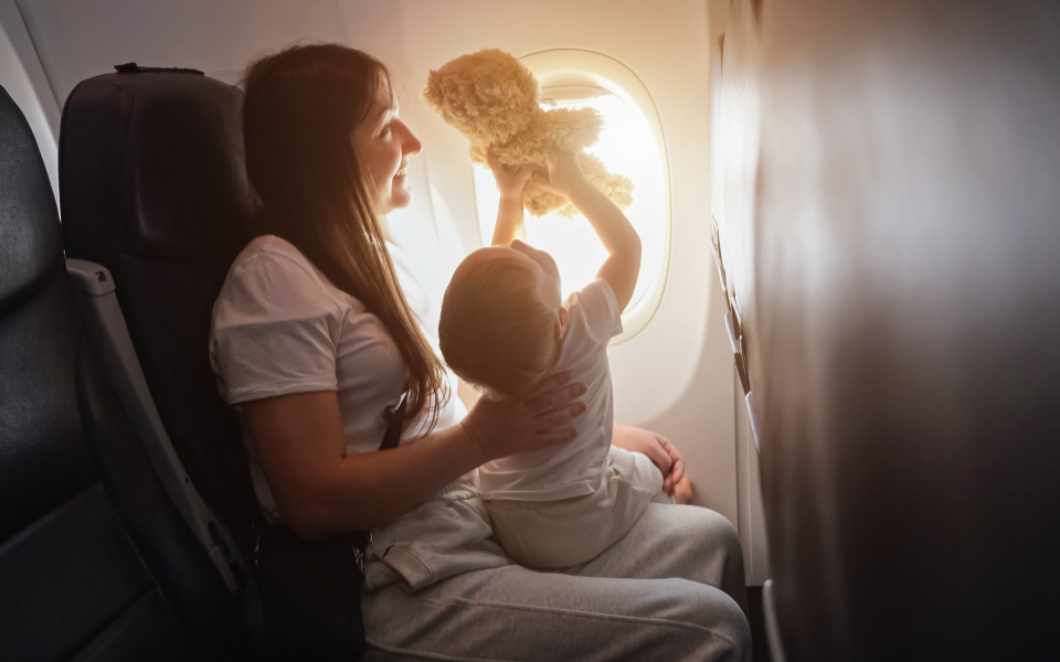 Mutter und Kind im Flugzeug, das Kind zeigt mit einem Stofftier aus dem Fenster.