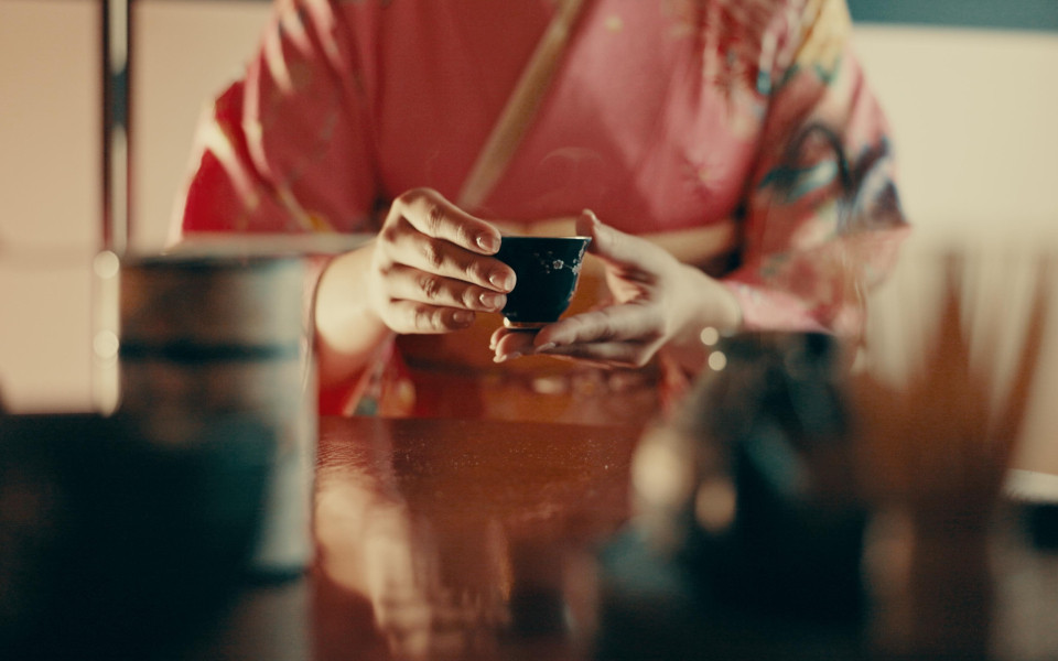 H&auml;nde einer Frau halten ein Matcha-Getr&auml;nk in einem traditionellen japanischen Teehaus