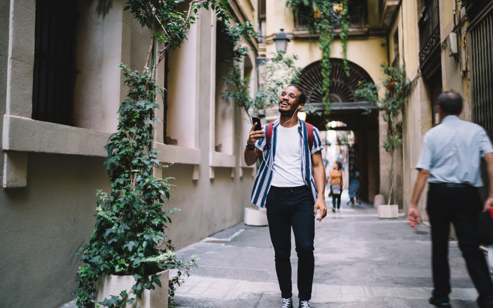 Mann mit Kopfh&ouml;rern und Smartphone spaziert durch eine Altstadtgasse und nutzt einen Audioguide.