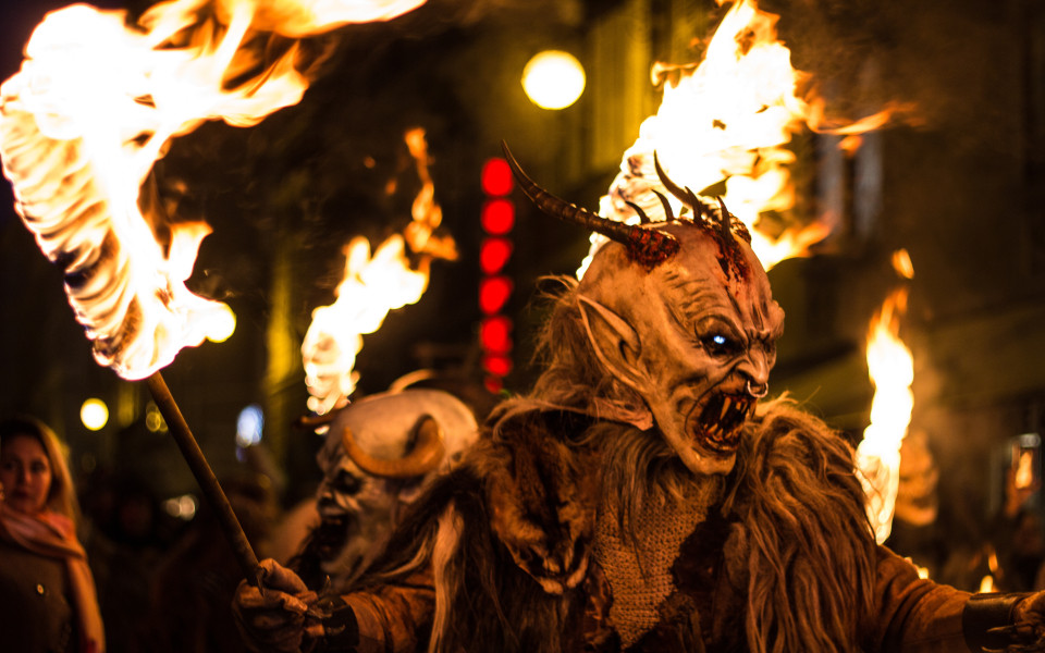 Krampus mit furchteinflößender Maske und Fackel beim traditionellen Krampuslauf in den Alpen.